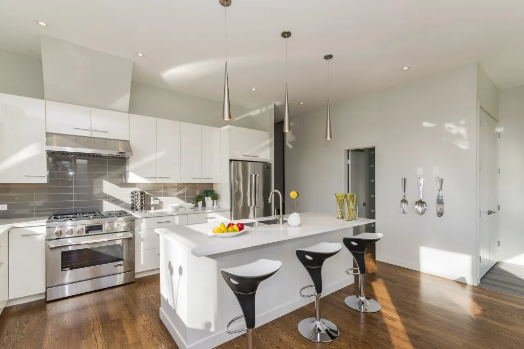 Una cocina moderna y elegante con una isla blanca elegante, electrodomésticos de acero inoxidable, iluminación colgante y elegantes taburetes de bar