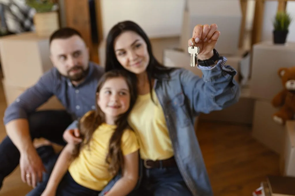 Una familia feliz en su nuevo hogar, con una madre sonriente sosteniendo un juego de llaves, que simboliza una compra o alquiler de propiedad exitosa.